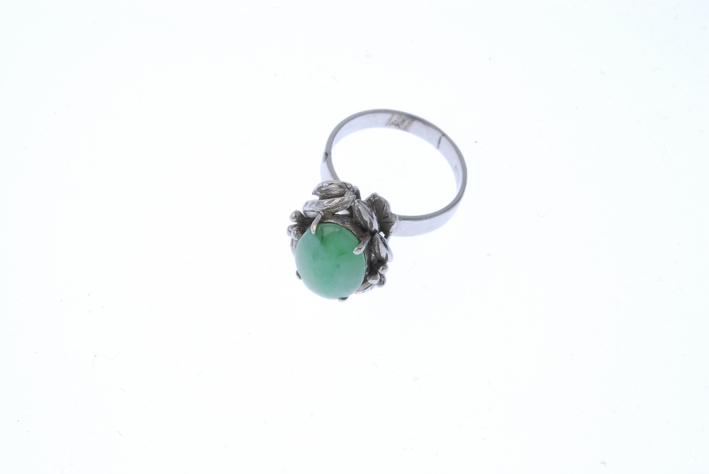 A jadeite dress ring. The oval jadeite cabochon, within a foliate surround, to the plain band. - Image 2 of 4