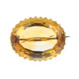 A citrine single-stone brooch. The oval-shape citrine, to the scrolling surmount. Length 2.5cms.