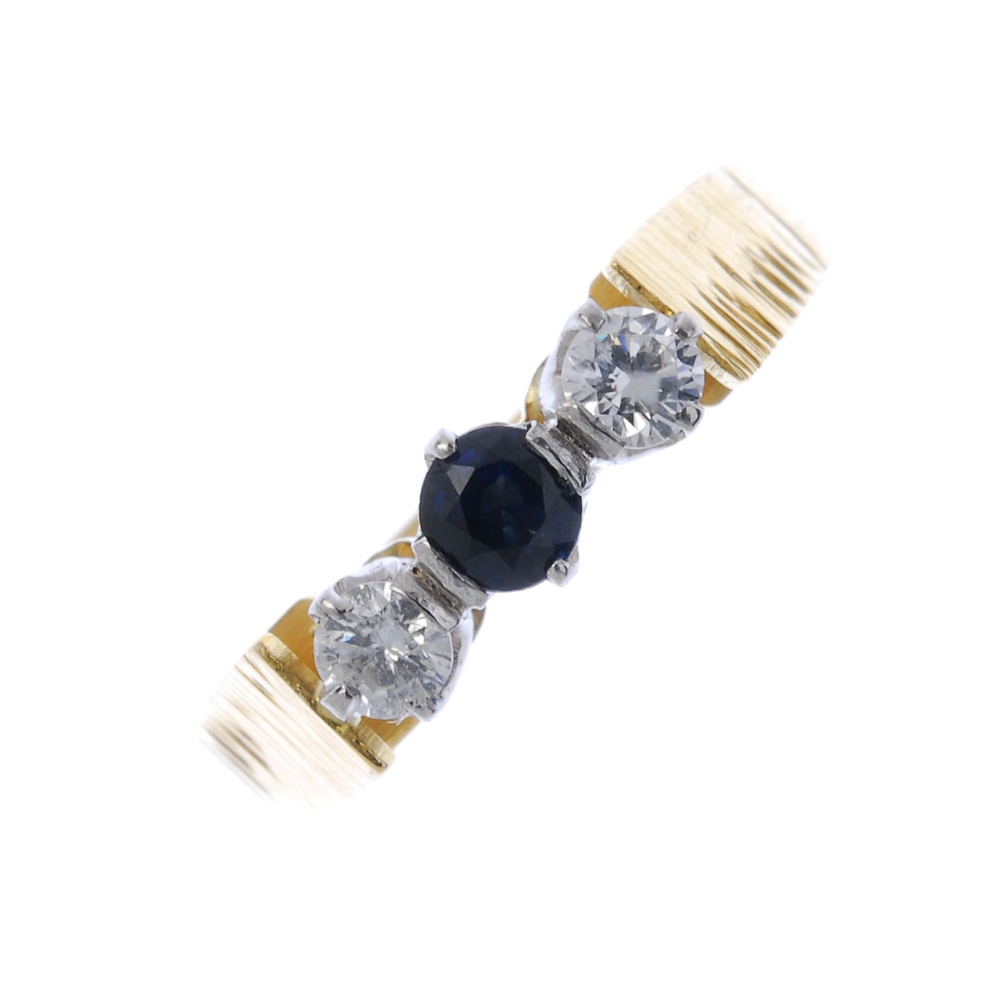 An 18ct gold sapphire and diamond three-stone ring. The circular-shape sapphire and brilliant-cut