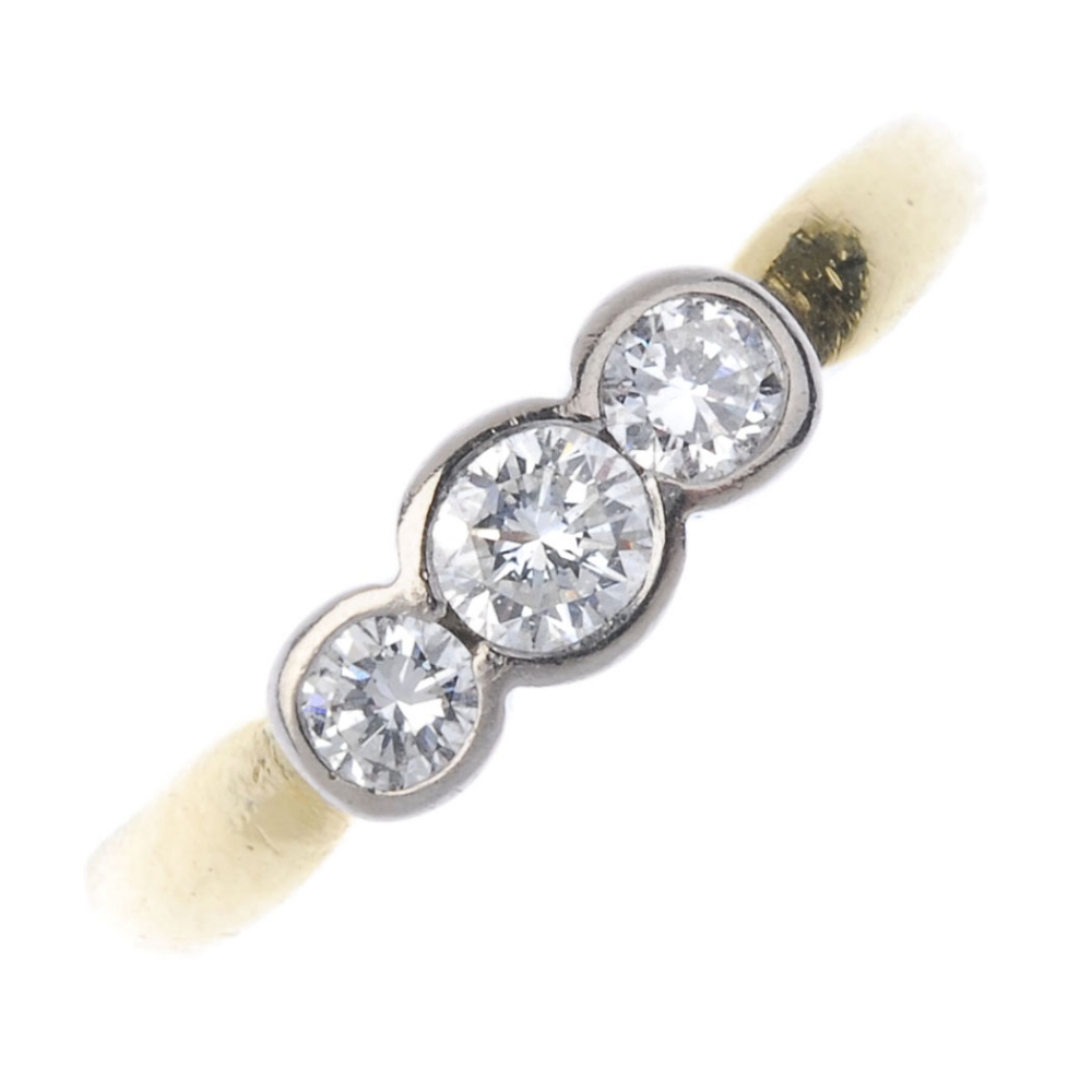 An 18ct gold diamond three-stone ring. Of bi-colour design, the graduated brilliant-cut diamond