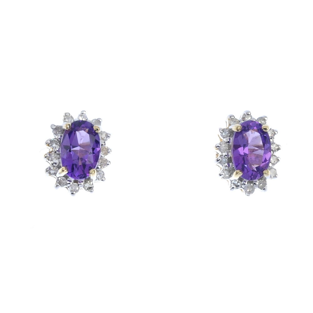 A pair of amethyst and diamond cluster ear studs. Each designed as an oval-shape amethyst, within