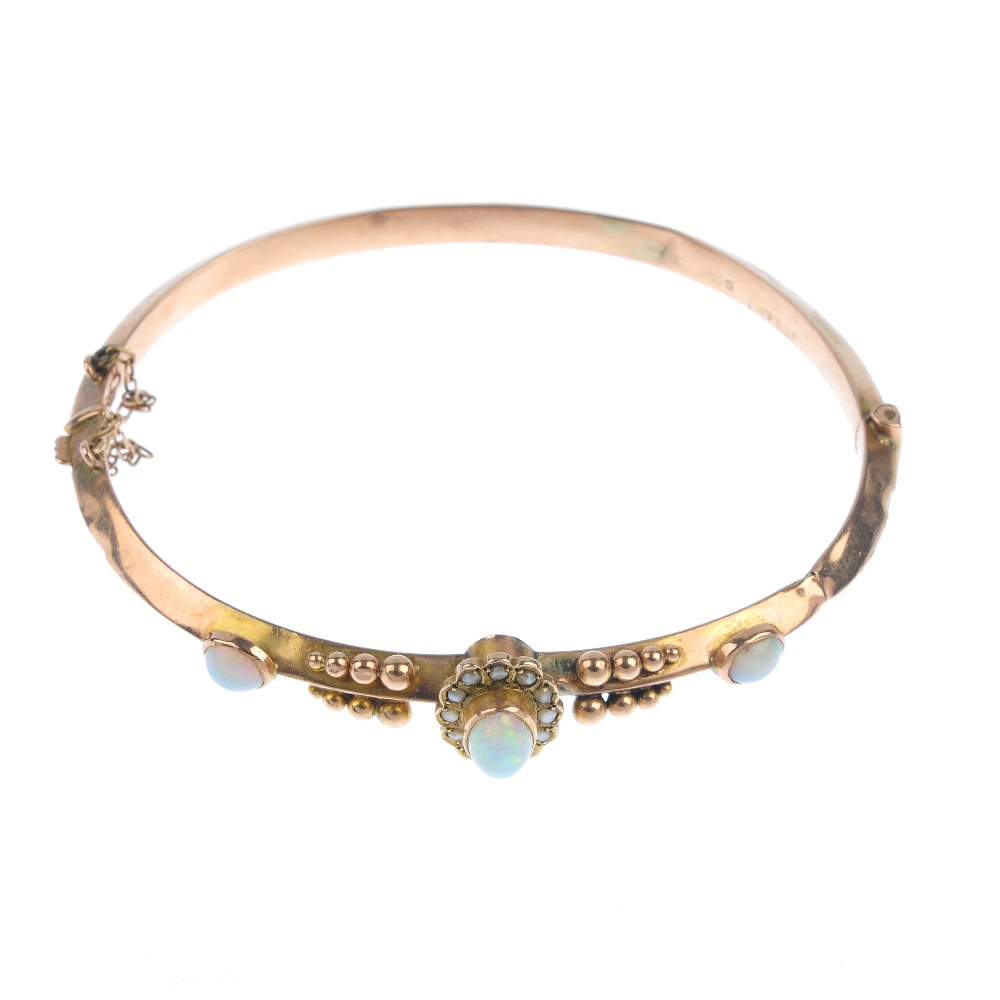 A late Victorian 9ct gold opal and split pearl hinged bangle. The oval opal cabochon and split pearl