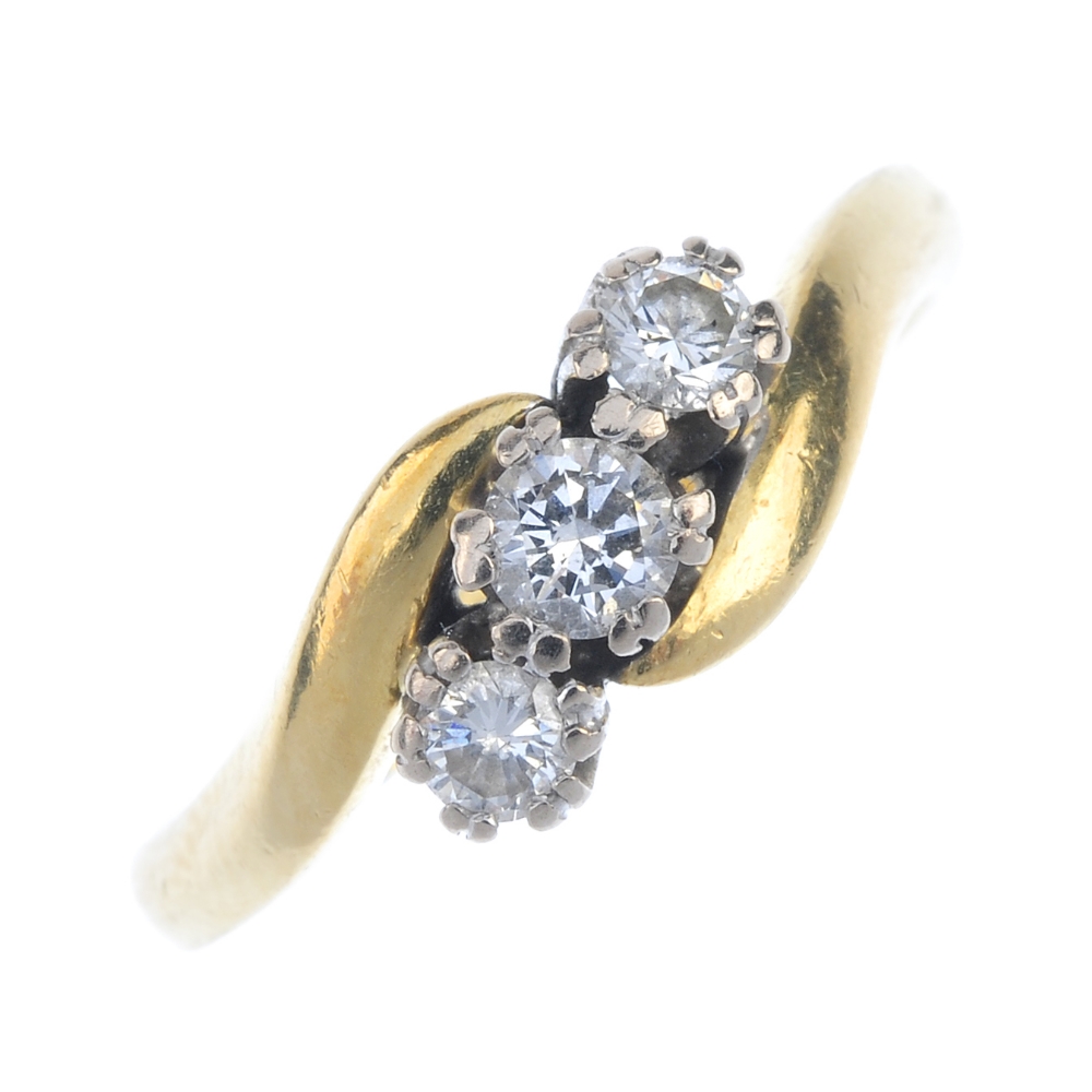 An 18ct gold diamond three-stone ring. The graduated brilliant-cut diamond diagonal line, to the