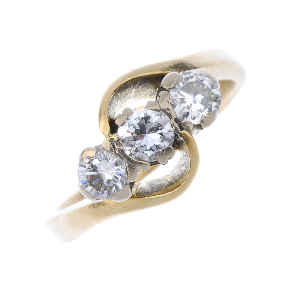 A diamond three-stone ring. The brilliant-cut diamond line, to the asymmetric sides and plain