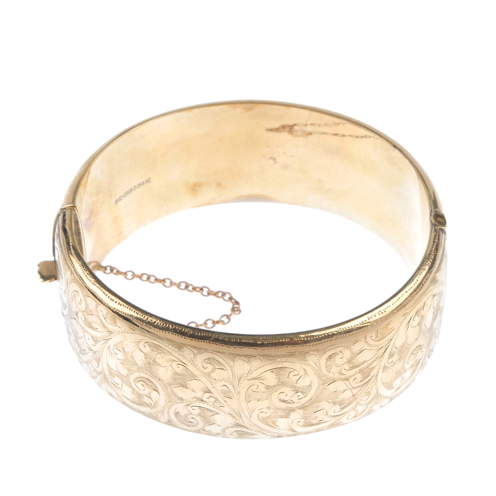 A mid 20th century 9ct gold hinged bangle. The hollow bangle, with foliate and scroll motif, to