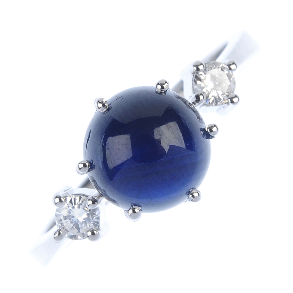 A sapphire and diamond three-stone ring. The circular sapphire cabochon, to the brilliant-cut