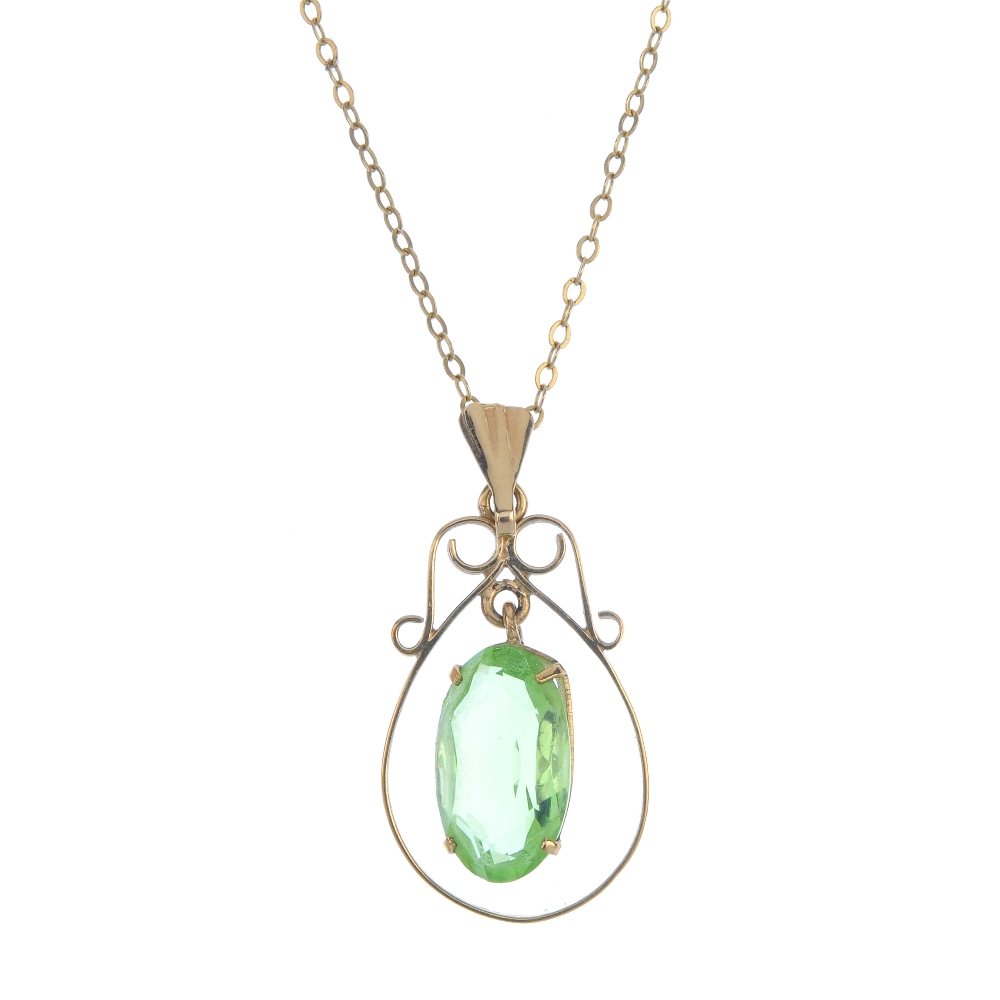 A 9ct gold paste single-stone pendant. The oval-shape green paste drop, suspended within a scroll