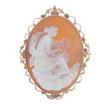 A cameo brooch. The shell carved to depict a goddess sitting on a cloud, playing a lyre, to the
