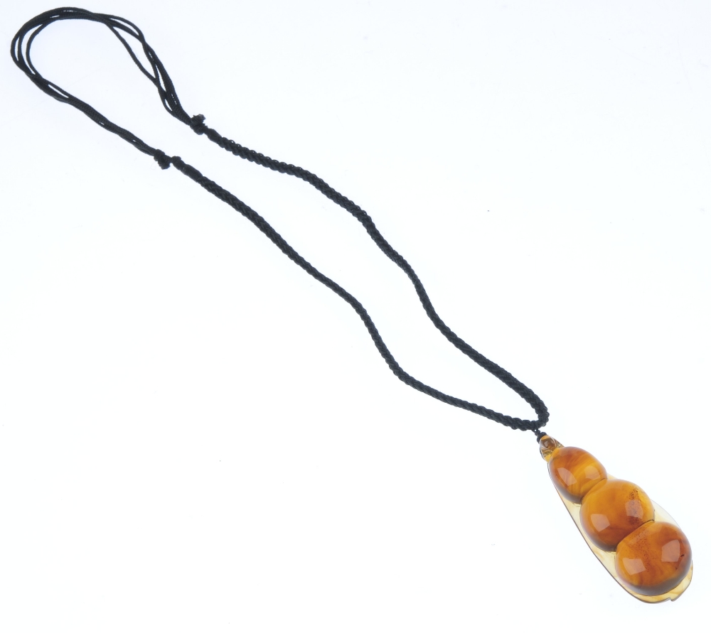 A natural Burmese amber pendant carved as a pea pod. The plaited black cord suspending the pear- - Image 3 of 3
