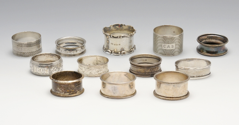 A selection of eleven assorted silver napkin rings and one plated example, of varying shapes and