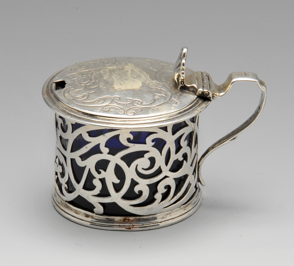 An early Victorian silver mustard pot with blue glass liner, the circular form with foliate scroll