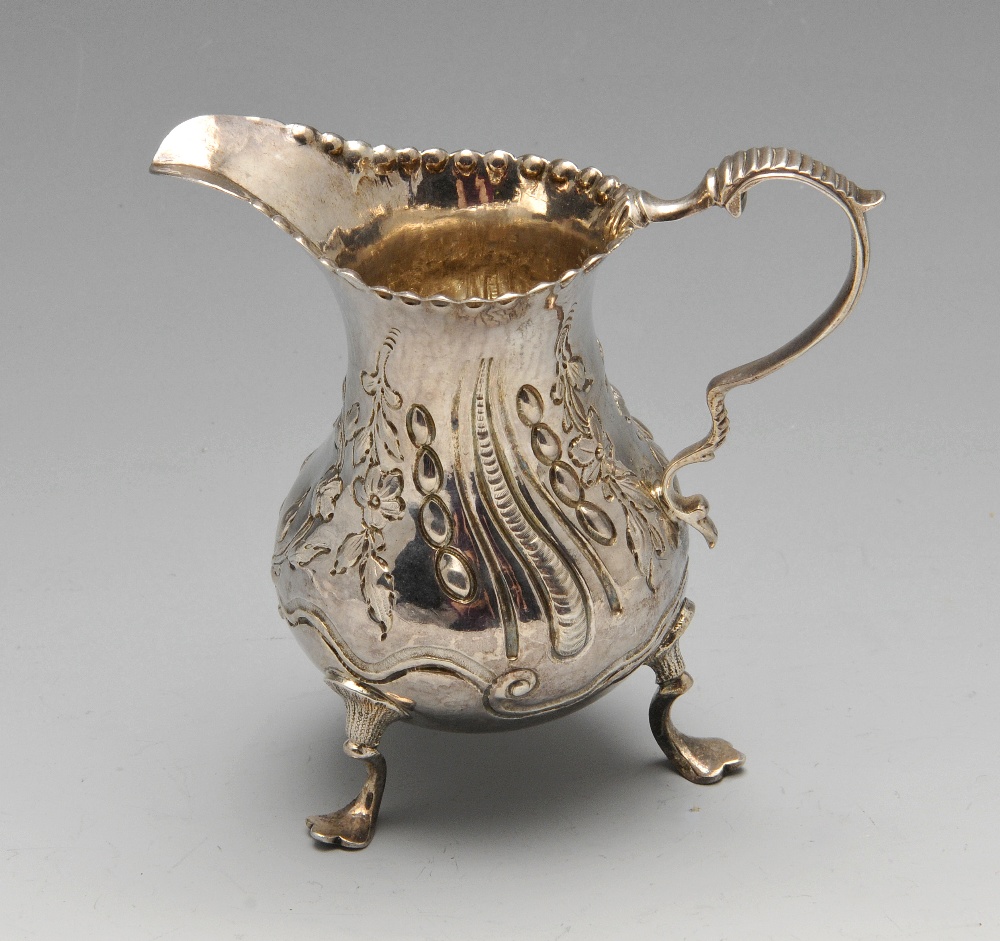 A George III silver cream jug, the bellied form with oblique fluting and beading amidst floral