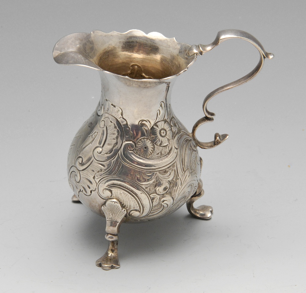 A George II silver cream jug of bulbous form with floral embossing surrounding an engraved crest,