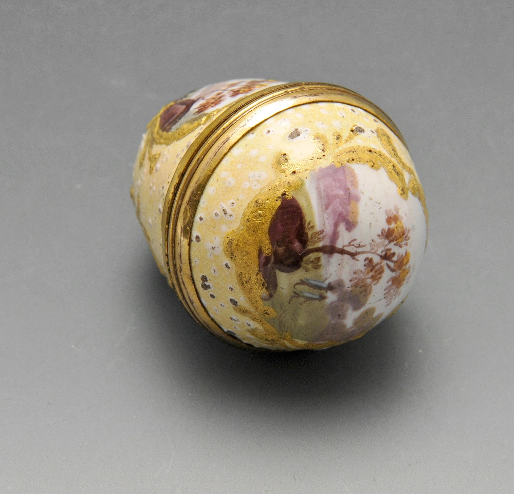 An enamel nutmeg grater of ovoid form, with gold tone mounts and gilt borders surrounding painted