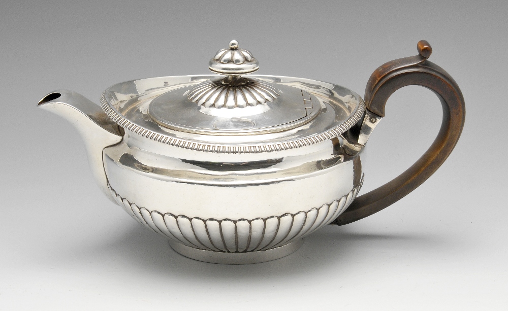 A George III silver teapot, the circular body part fluted, rising to the gadrooned rim and similarly