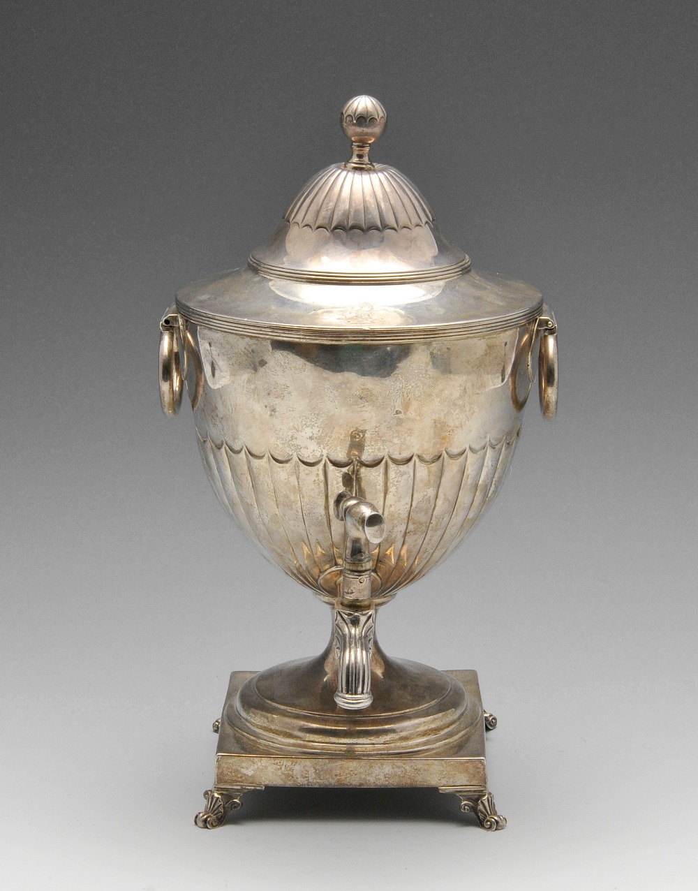 A George III silver tea urn, the crested urn form with twin hinged loop handles, part fluted body