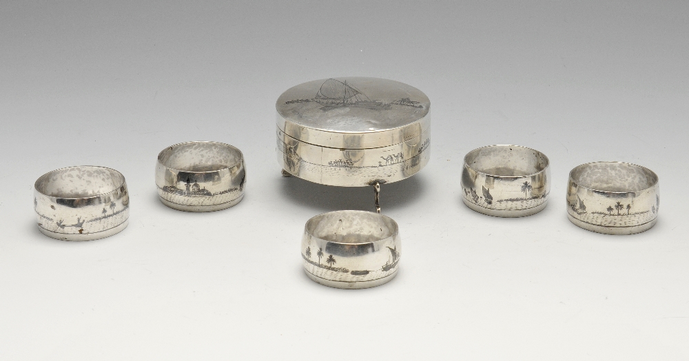 A white metal trinket box of circular form raised on three scroll feet, and five similar napkin