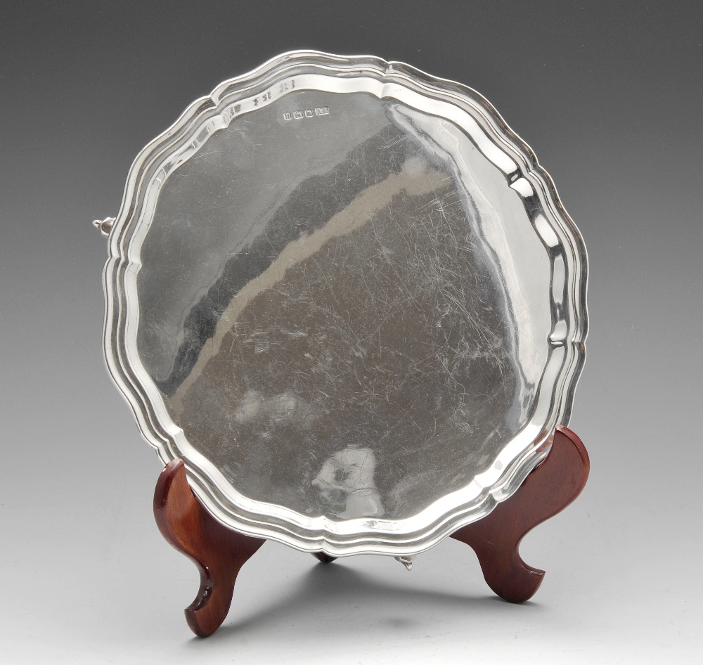 A modern silver salver the circular form with raised and shaped edge and standing on three scroll