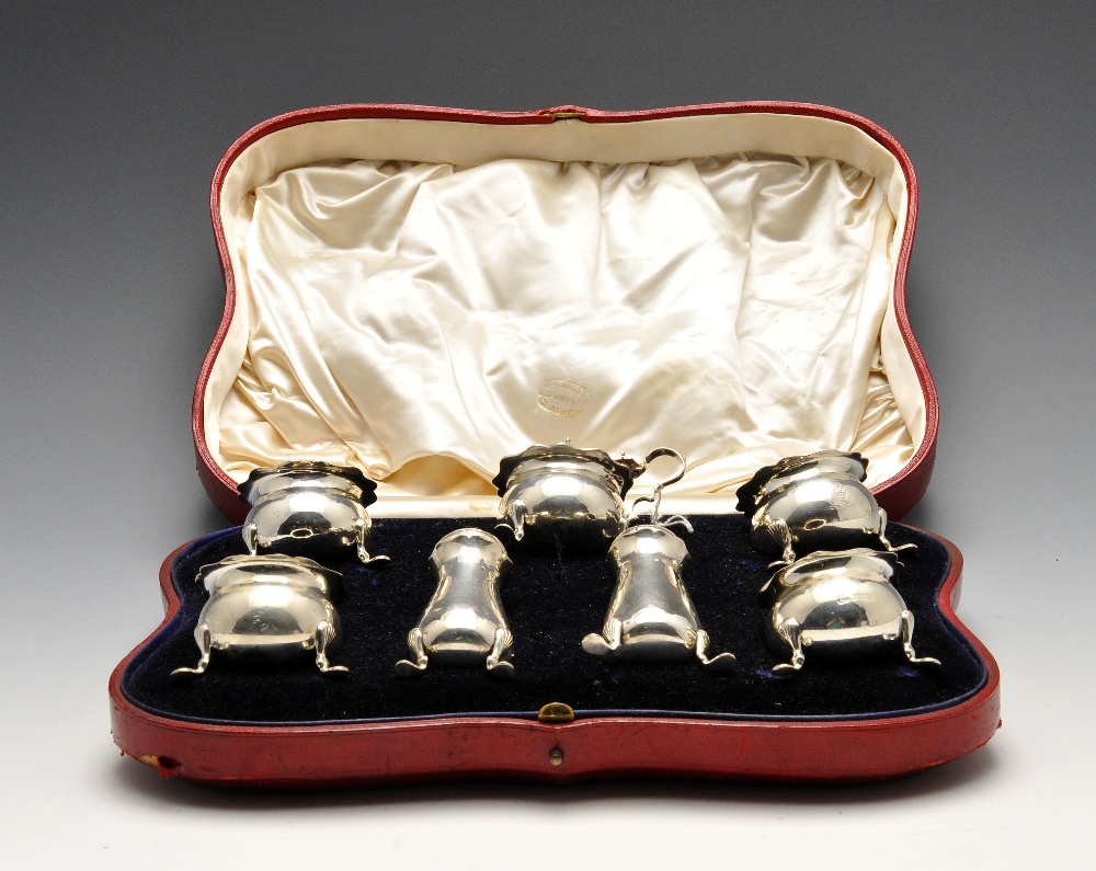 An Edwardian cased seven piece silver condiment set, of bellied form with engraved crest and