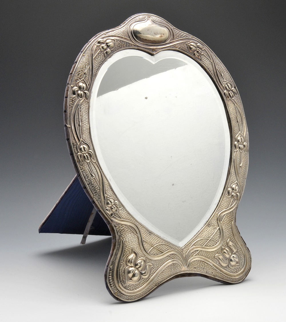 An Edwardian Art Nouveau silver mounted mirror with easel back, the heart shape bevelled glass plate