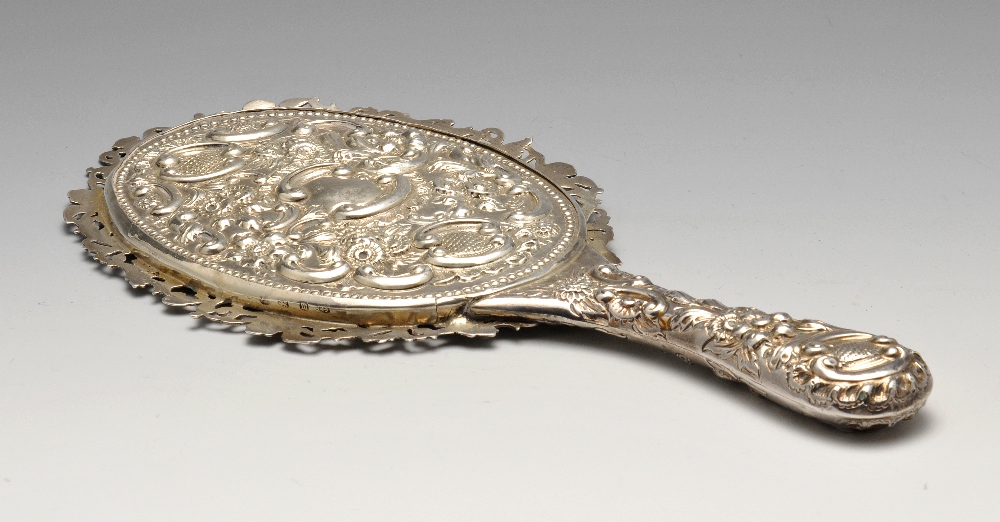 A late Victorian silver mounted hand mirror, the oval bevelled glass plate within an ornately