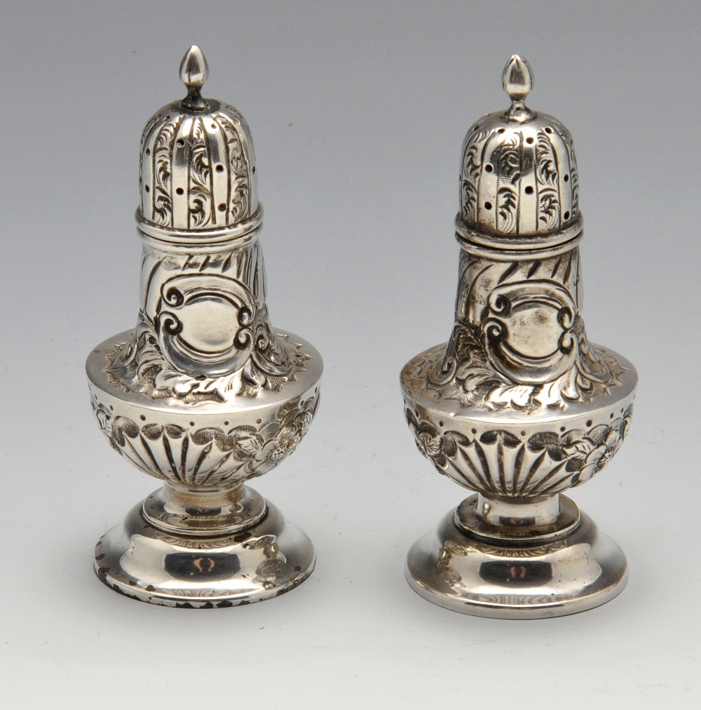 A pair of late Victorian silver pepper pots, each of bellied form to a footed base and embossed with