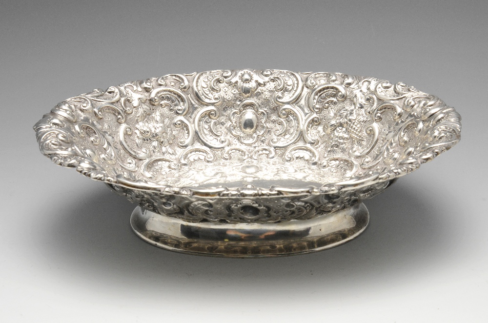 A Victorian silver dish of oval form, entirely embossed with fruiting and floral scrolls upon a