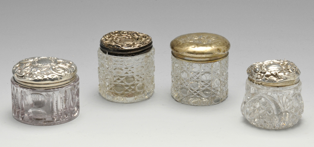 Four assorted Edwardian and later silver topped glass vanity jars of circular form, one lid