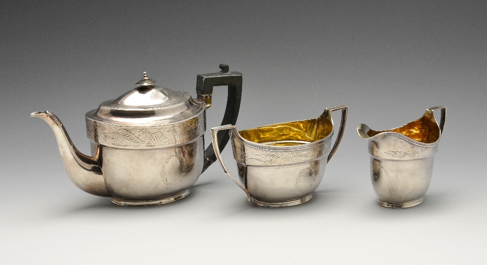 A George III silver three piece silver tea service, the oval form engraved with foliate fruiting