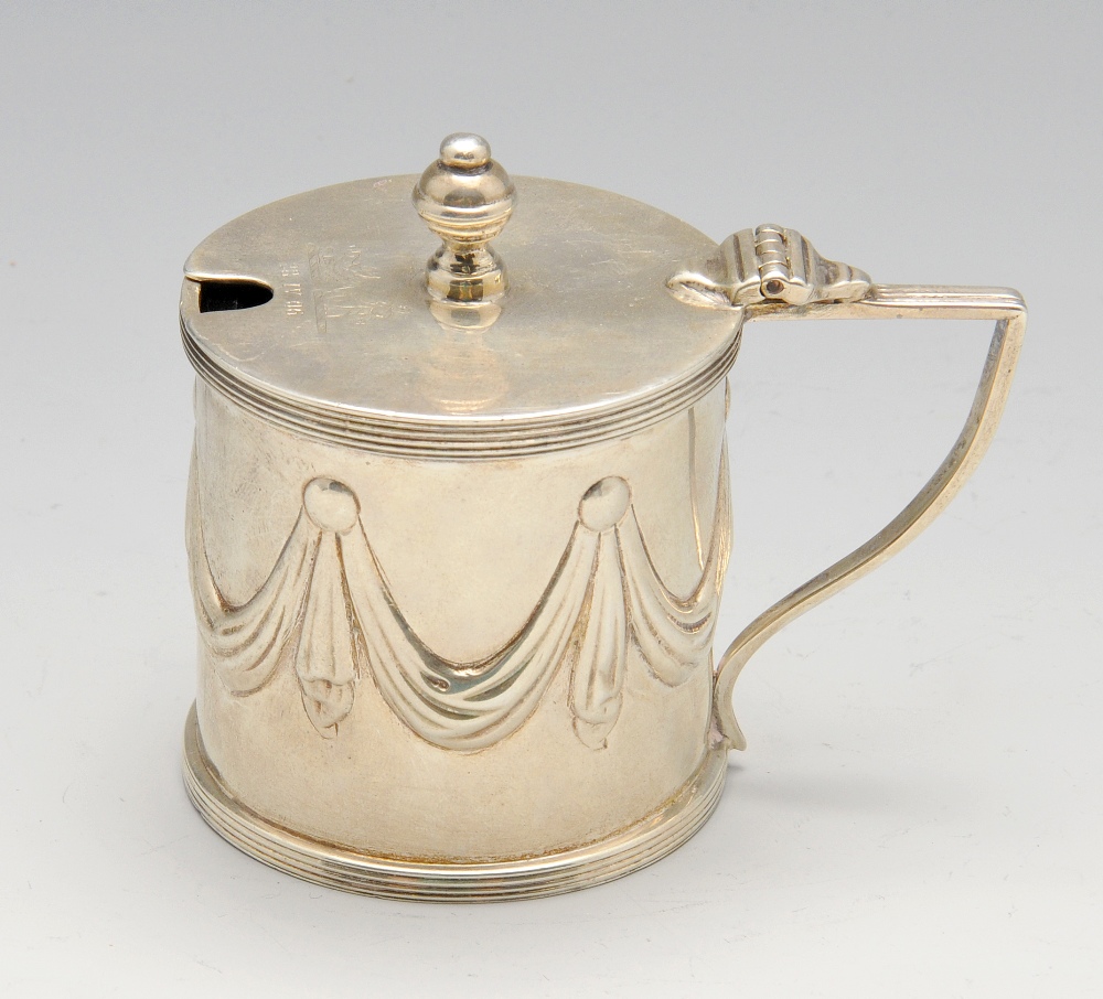 An Edwardian silver mustard pot, the drum form embossed with swags within reeded borders, hinged