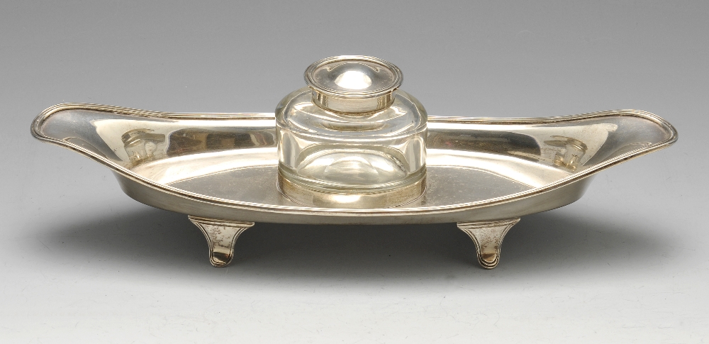 An early twentieth century silver inkstand of elongated oval form with reeded rim and raised on four