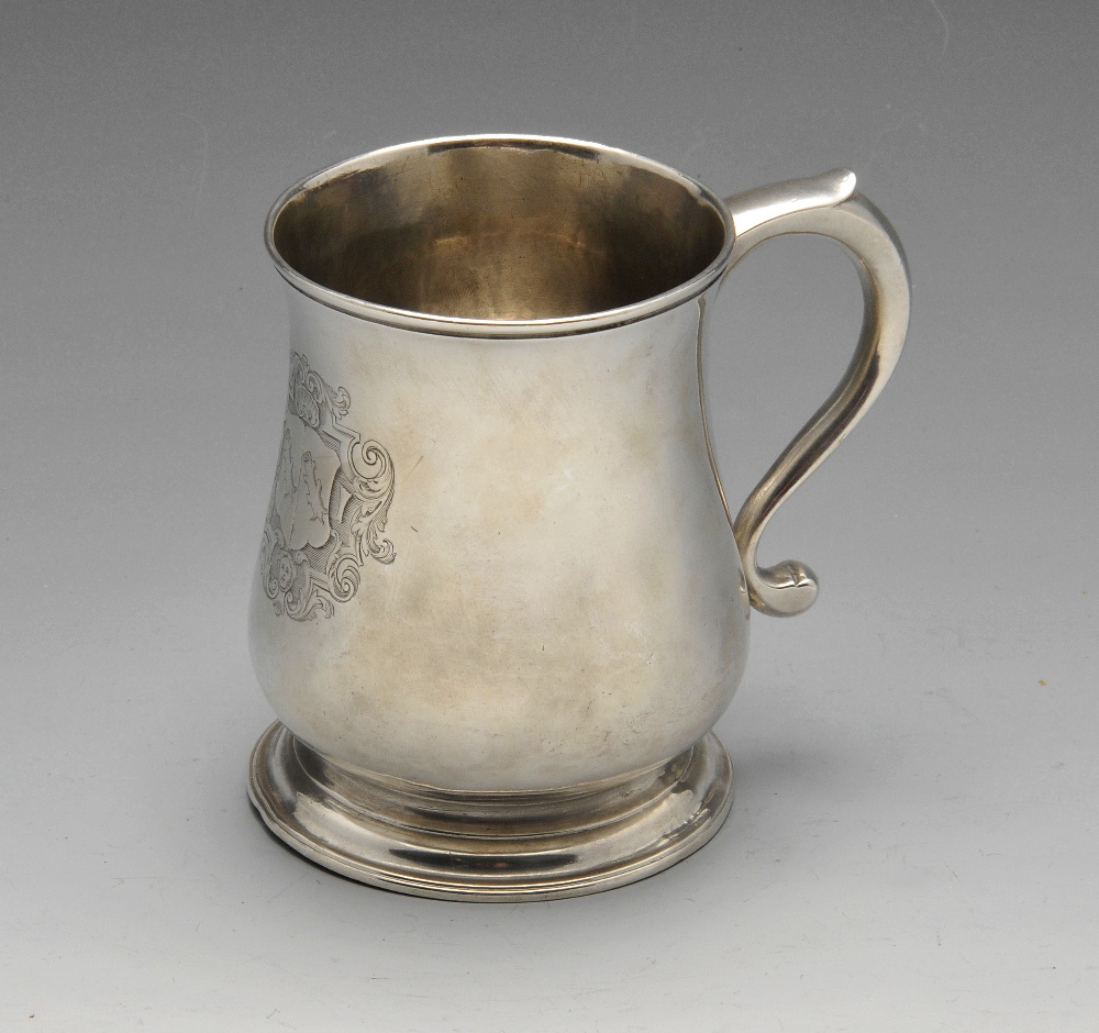 A George II silver mug of baluster form, crested and standing on a spread circular foot.