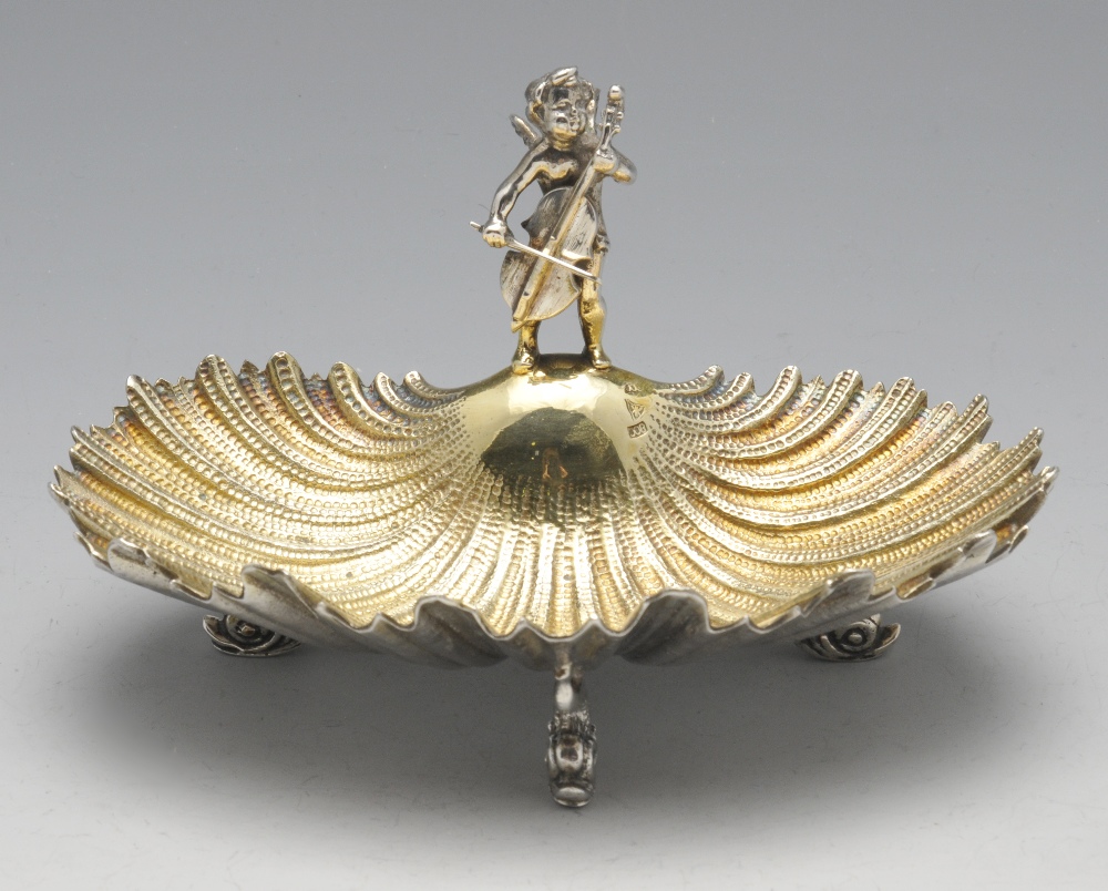 A small continental shell dish raised on three stylised dolphin feet and having a figural mount