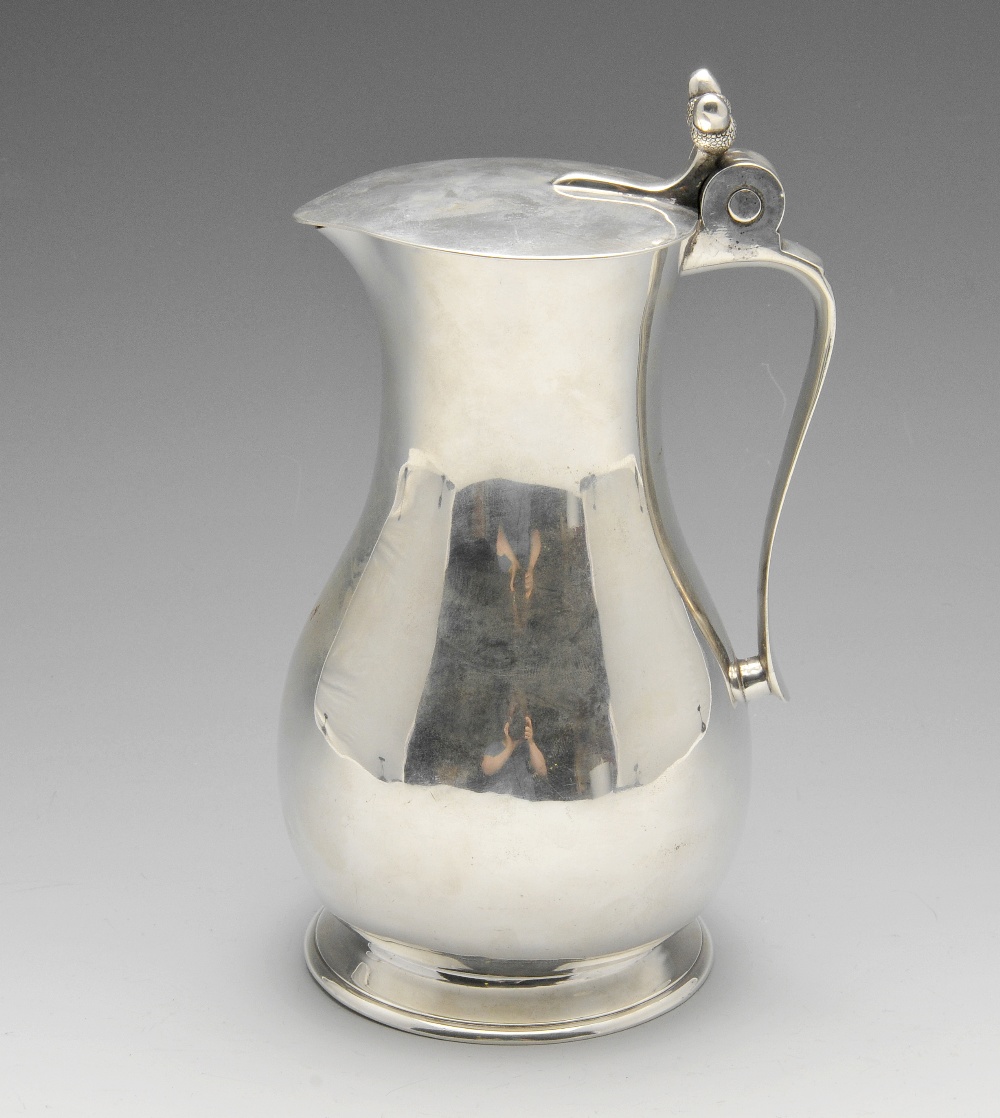 An Edwardian silver lidded jug, the plain bellied form standing on a circular foot with slightly