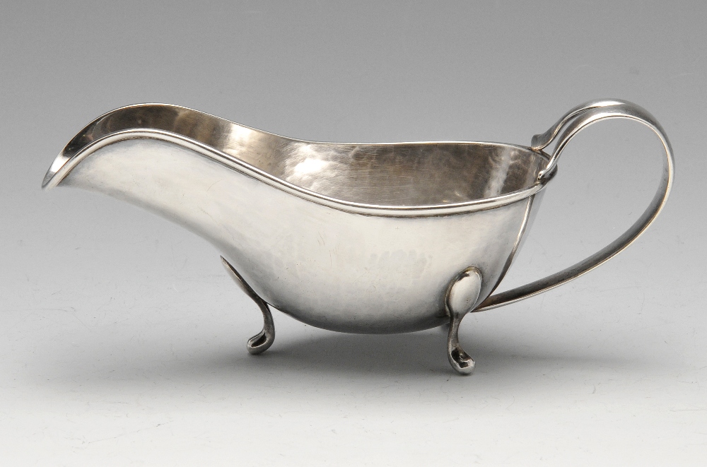 An Italian silver sauce boat of planished form with moulded rim, split loop handle and raised on