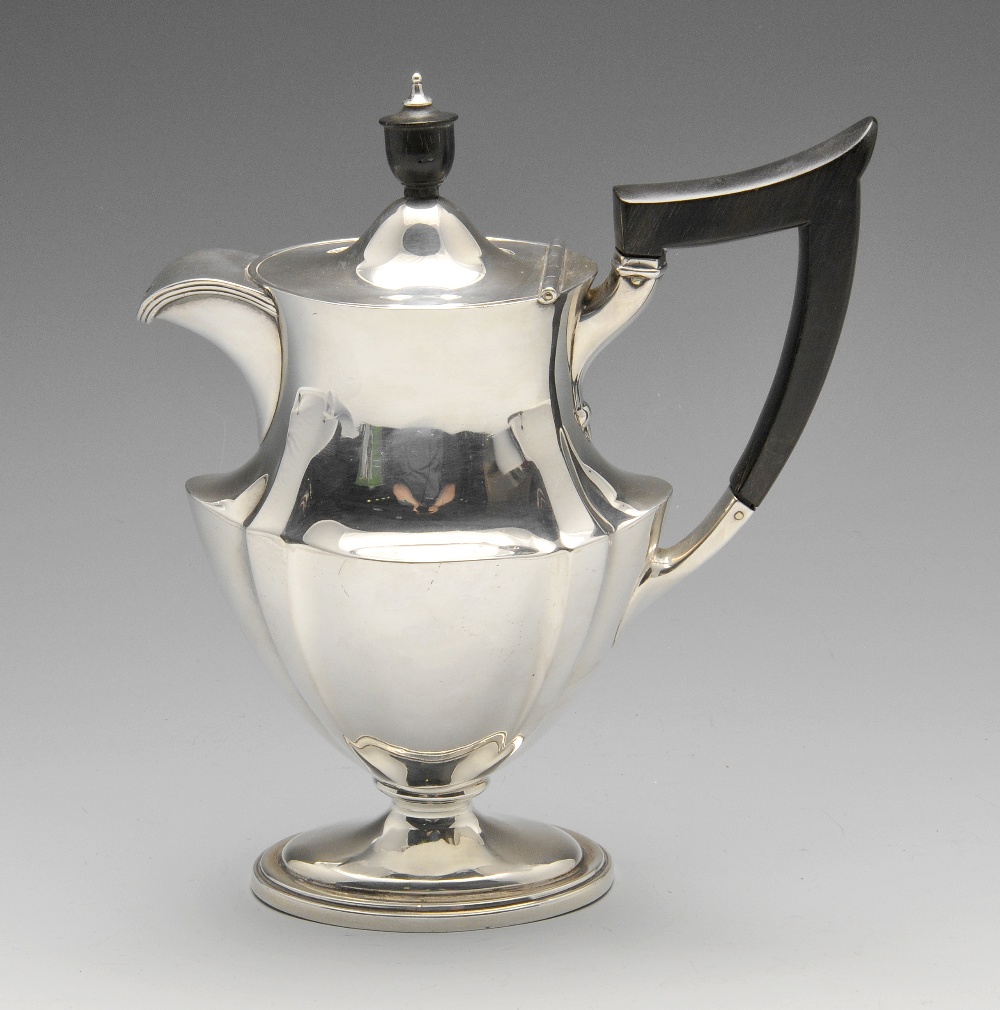 An Edwardian silver hot water pot, the oval waisted body with fluted corners and ebonised handle and