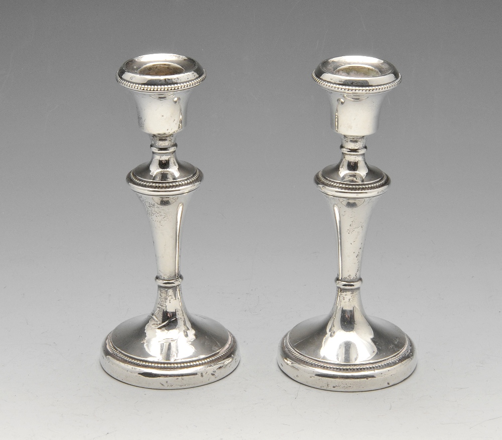 A pair of 1930's silver mounted candlesticks, each with beaded borders and a filled circular base