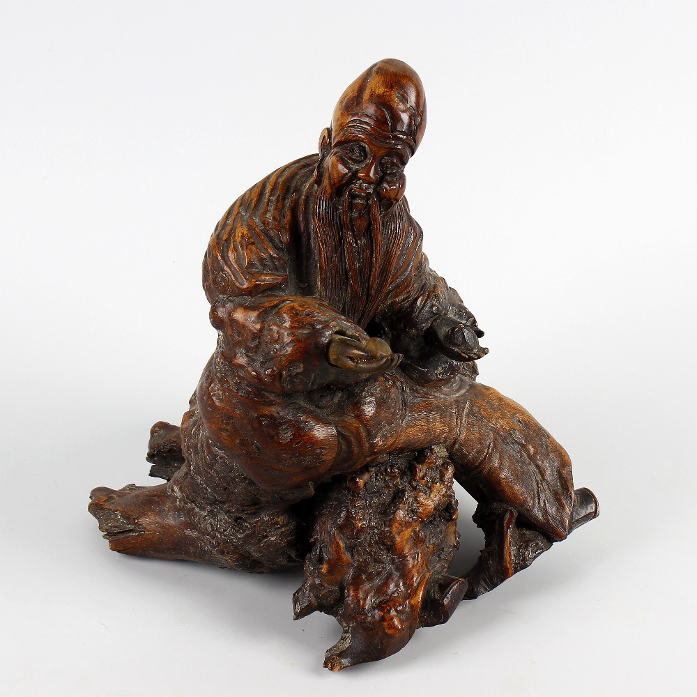 A 19th century Oriental carved rootwood figure. Modelled as a sage or Immortal, holding a peach