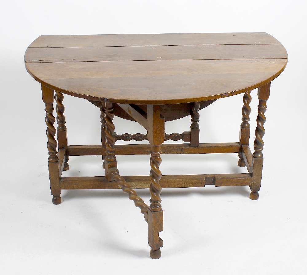 An oak drop leaf gateleg table. The oval top above single frieze drawer and false drawer, raised