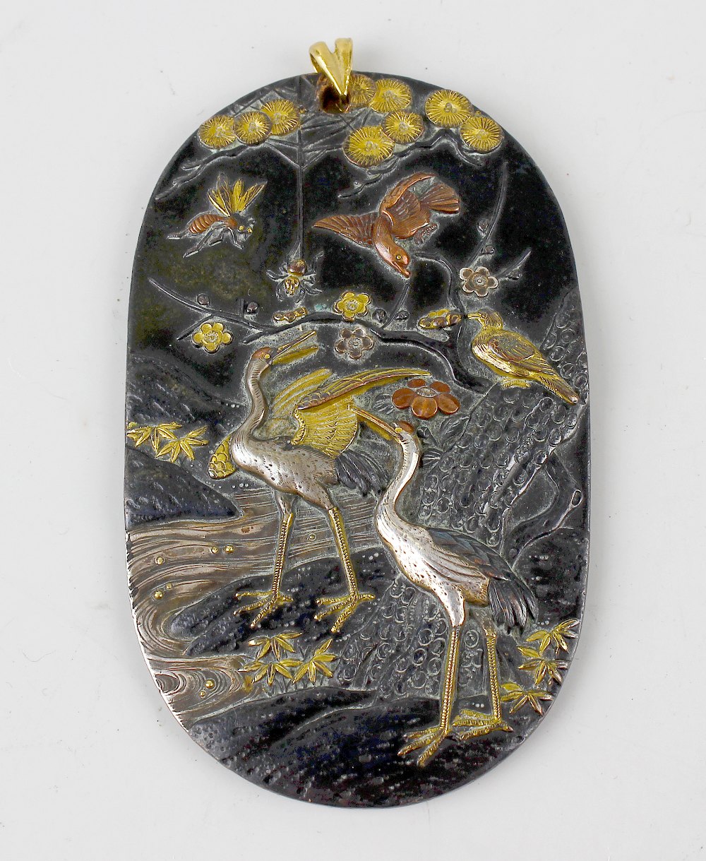 A Japanese shakudo pendant, of oval outline finely decorated with scene of two cranes beside a
