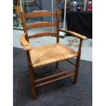 Unknown - An oak ladderback chair with woven grass seat and a stretcher frame, width 63cm.