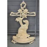 A white painted cast iron umbrella stand in the form of a seated dog near a tree stump,