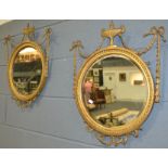 A pair of circular gilt wall mirrors each surmounted with an urn pediment and bordered with ribbons