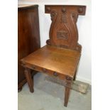 A pair of mid 19th Century oak hall chairs the carved backs centred with a dog holding a spear