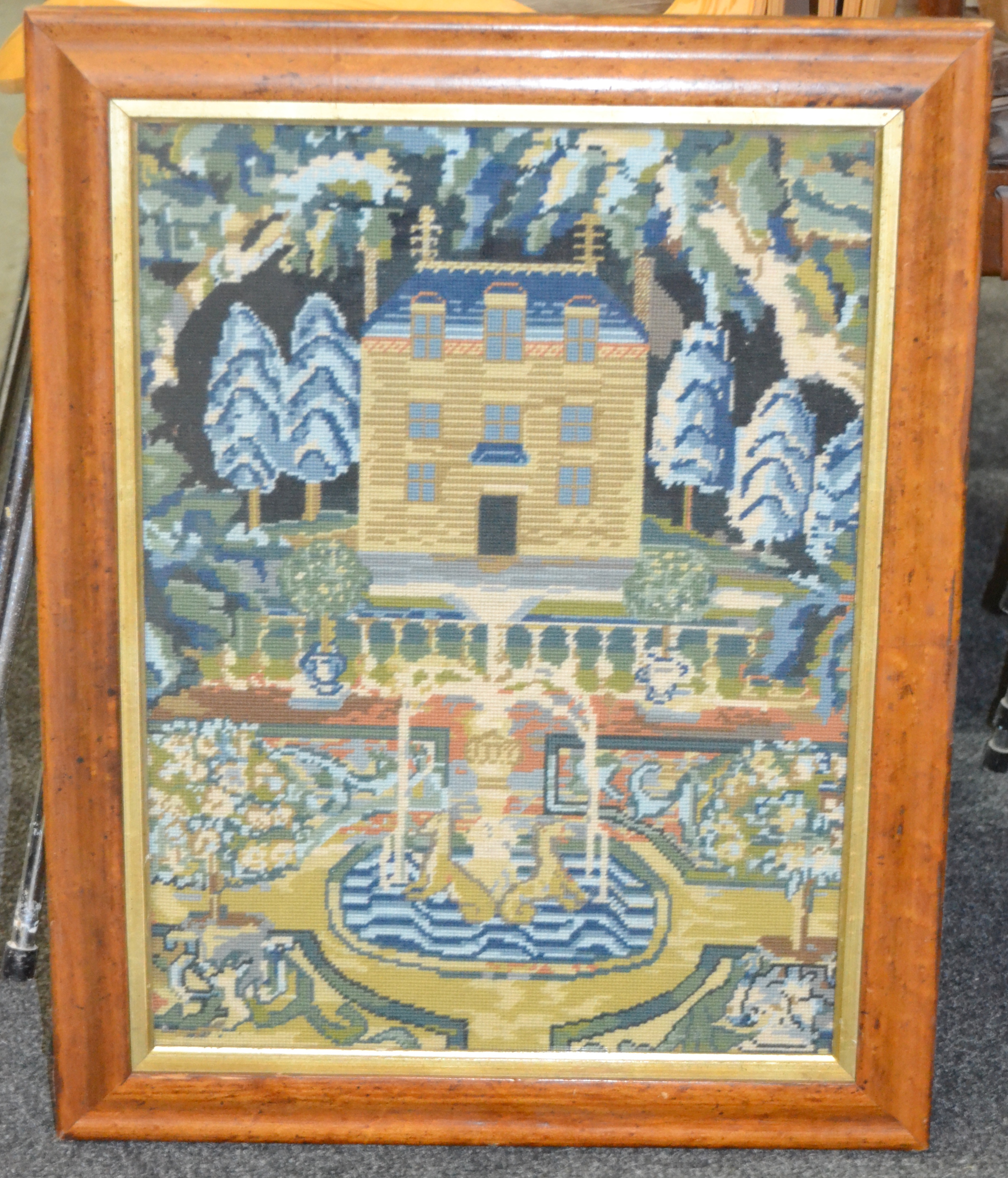 A 20th Century woolwork sampler depicting a Georgian house above a pool and fountain within a maple