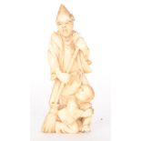 A late 19th to early 20th Century Japanese carved ivory figure of man wearing a pointed hat holding