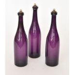 A set of three late 18th Century amethyst glass decanters of slender bottle form with annulated