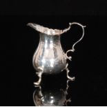 A Georgian hallmarked silver cream jug of baluster form with broken scroll handle and raised on