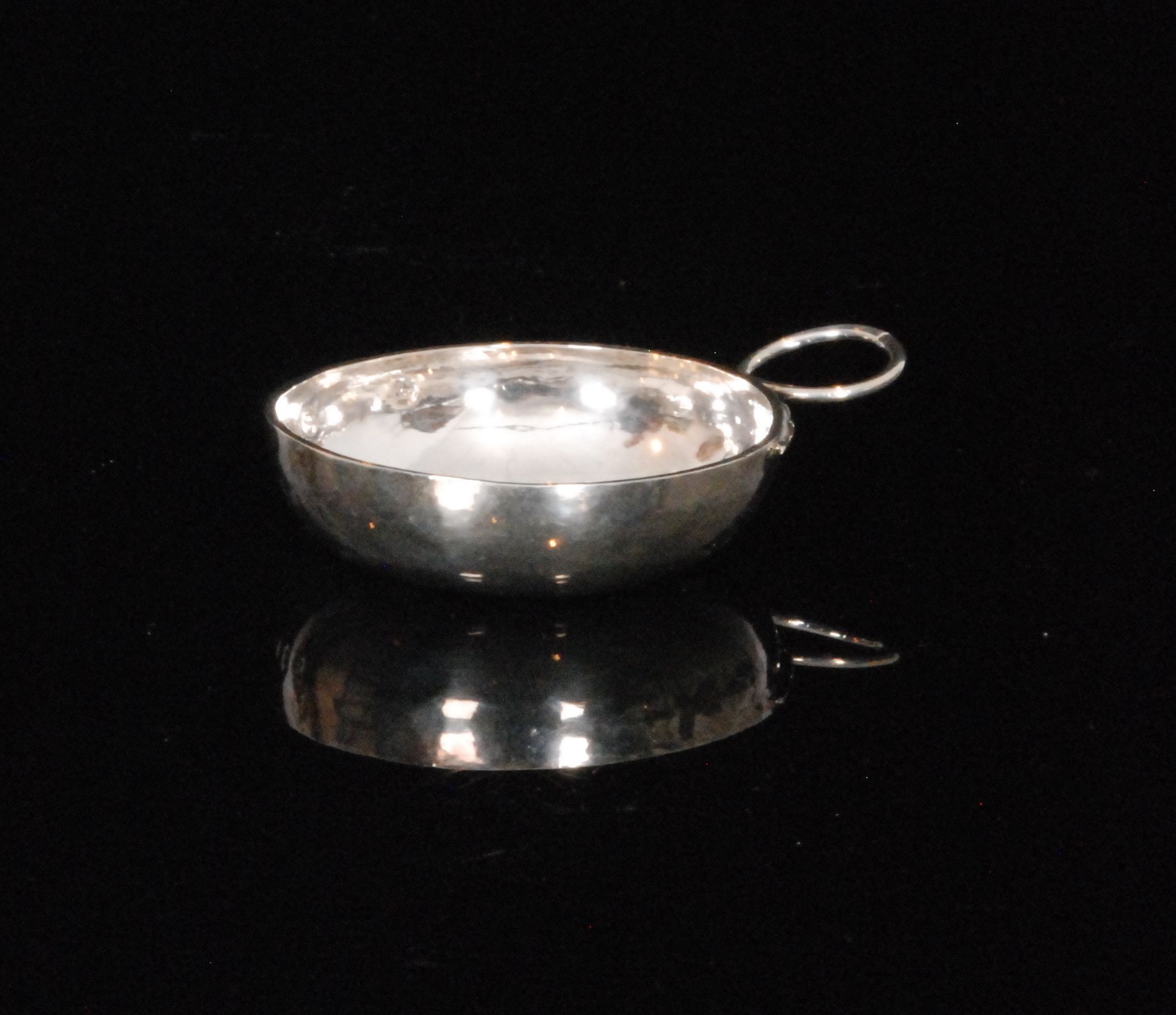 A late 19th to early 20th Century French silver wine taster of plain circular form with whiplash