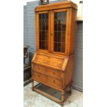 A 1920s oak bureau bookcase enclosed by a pair of coloured leaded light doors over a geometric fall